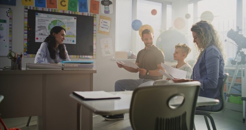 Parents meeting with a teacher in a classroom to discuss student progress and school activities